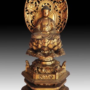 Puede incluir: Una estatua dorada de Buda en posición de meditación sentado. La estatua está sobre una base de varios niveles con intrincadas tallas y un fondo decorativo. La estatua mide aproximadamente 46 cm de altura.