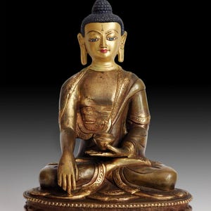 May include: A seated bronze Buddha statue with a gold-coloured face and robes. The statue is in a meditative pose, holding a small bowl. The base is intricately detailed with a lotus flower design. The statue is approximately 30 cm tall.