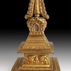 May include: A gold-colored, ornate stupa with intricate carvings. The stupa features a tiered base, detailed relief work, and a spire-like top with swirling patterns. A small, red-colored element is visible within the structure.