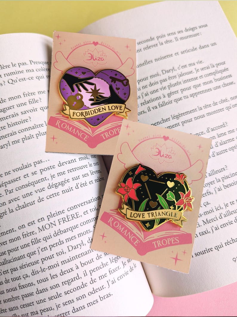 May include: Two heart-shaped enamel pins with gold trim. One features a purple heart with hands reaching for a star, the text "Forbidden Love", and the word "Romance". The other has a black heart with red flowers and the text "Love Triangle".