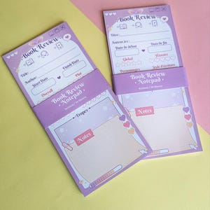 Op de afbeelding: Twee paarse "Book Review Notepad" notitieblokken tegen een lichtroze en gele achtergrond. Elk notitieblok heeft een omslag met "Book Review" en ruimtes voor titel, auteur en data. De notitieblokken zijn 9x20cm en bevatten 30 vellen.