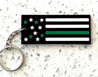 May include: A black and white American flag keychain with a green stripe, representing the thin green line, and a silver key ring.