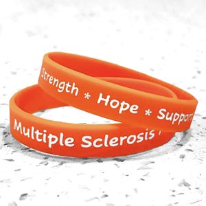 May include: Two orange silicone wristbands stacked on top of each other. The top band features the white text "Strength * Hope * Support" and the bottom band features the white text "Multiple Sclerosis" printed in a clear, sans-serif font.