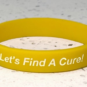 May include: Yellow rubber bracelet with the text "Let's Find A Cure!" printed in white.