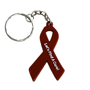 May include: A maroon ribbon keychain with a silver key ring and chain. The ribbon has the text "Let's Find A Cure!" printed on it in white.