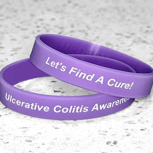May include: Two purple silicone wristbands with white text. The top band reads "Let's Find A Cure!" and the bottom band reads "Ulcerative Colitis Awareness".