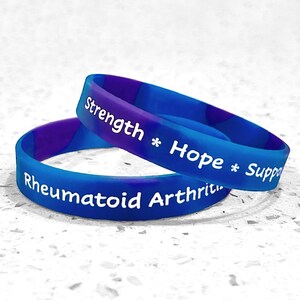 May include: Two blue and purple swirl silicone wristbands. One band features the white text "Strength * Hope * Support" and the other band features the white text "Rheumatoid Arthritis". The bands are stacked on top of each other in a circular shape.