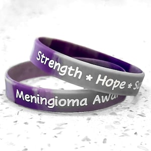 May include: Two silicone wristbands, one stacked on top of the other. The top band is gray with purple marbling and the words "Strength * Hope *" in white. The bottom band is purple and gray with "Meningioma Aware" in white.