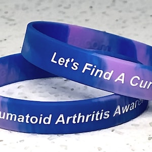 May include: Two blue and pink silicone wristbands with white text. The top band reads "Let's Find A Cure!" and the bottom band reads "Rheumatoid Arthritis Awareness".