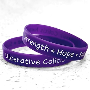 May include: Two purple rubber bracelets with white text. One bracelet reads "Strength * Hope * Support" and the other reads "Ulcerative Colitis Awareness". The bracelets are stacked on top of each other.