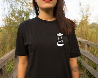 Könnte beinhalten: Ein schwarzes T-Shirt mit einem weißen Aufdruck einer Person, die von einem UFO entführt wird.