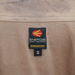 K&ouml;nnte beinhalten: Ein braunes Etikett mit dem Text "Energie jeans x-perience" und der Website "www.energie.it". Das Etikett hat auch ein schwarzes Pfeil-Logo und die Gr&ouml;&szlig;e "S" darauf.