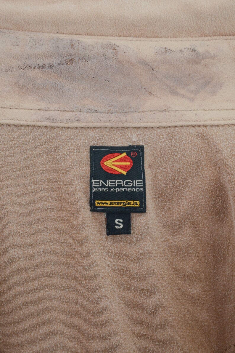K&ouml;nnte beinhalten: Ein braunes Etikett mit dem Text "Energie jeans x-perience" und der Website "www.energie.it". Das Etikett hat auch ein schwarzes Pfeil-Logo und die Gr&ouml;&szlig;e "S" darauf.