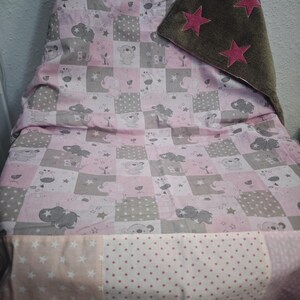 May include: A baby blanket with a patchwork design featuring pink, gray, and white squares. The squares are decorated with animal illustrations, stars, and polka dots. A brown blanket with pink star accents is folded over the top.