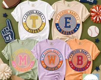 May include: Five short-sleeve t-shirts in white, beige, light green, lavender, and orange. Each shirt features a circular graphic with a large letter, the text SCHOOL NAME, and a team name: TIGERS, EAGLES, MUSTANGS, WILDCATS, or BEARS.
