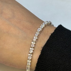 May include: A silver tennis bracelet with a row of round, clear diamonds.