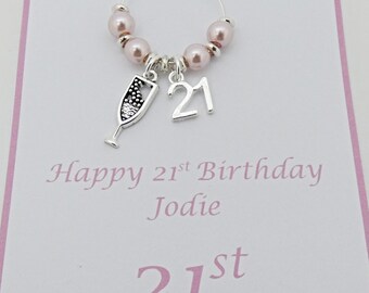 May include: A pink and silver 21st birthday wine charm with a champagne glass charm and a card that says "Happy 21st Birthday Jodie 21st"
