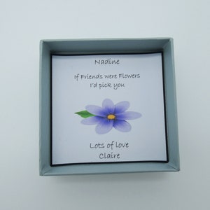 May include: A small blue box with a white card inside. The card has a purple flower and the text "Nadine, If Friends were Flowers I'd pick you, Lots of love Claire".