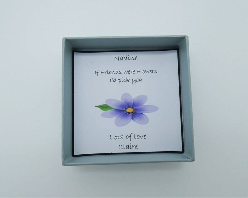 May include: A small blue box with a white card inside. The card has a purple flower and the text "Nadine, If Friends were Flowers I'd pick you, Lots of love Claire".