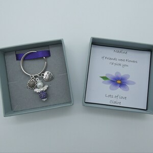 May include: A small gift box with a silver key chain inside. The keychain has a purple angel charm, a sunflower charm, and a heart charm that says "Best Friend". The box also includes a card that says "Nadine, If friends were flowers I'd pick you. Lots of love, Claire."