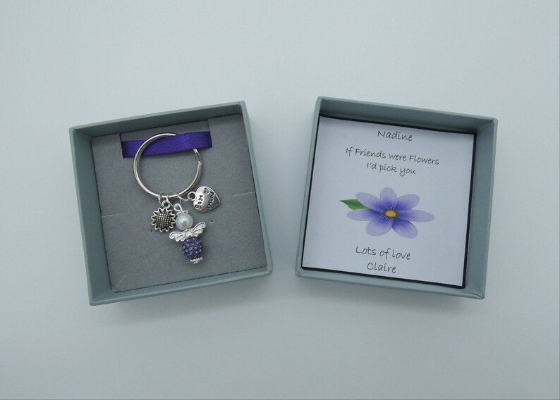 May include: A small gift box with a silver key chain inside. The keychain has a purple angel charm, a sunflower charm, and a heart charm that says "Best Friend". The box also includes a card that says "Nadine, If friends were flowers I'd pick you. Lots of love, Claire."
