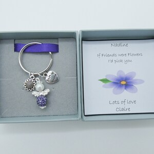 May include: A small gift box with a purple ribbon and a silver keychain with a purple angel charm, a sunflower charm, and a heart charm that says "Best Friend". The card inside the box reads "Nadine, If Friends were Flowers I'd pick you. Lots of love, Claire."