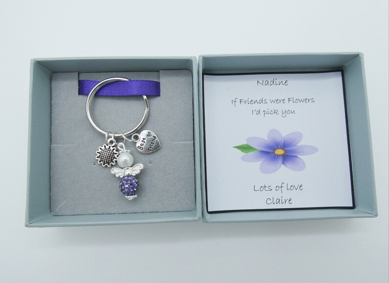 May include: A small gift box with a purple ribbon and a silver keychain with a purple angel charm, a sunflower charm, and a heart charm that says "Best Friend". The card inside the box reads "Nadine, If Friends were Flowers I'd pick you. Lots of love, Claire."