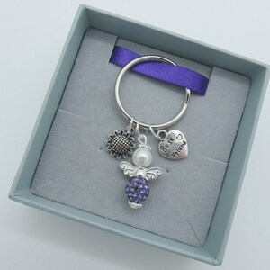 May include: A silver key chain with a purple crystal angel charm, a sunflower charm, a pearl bead, and a heart charm that says "Best Friend".