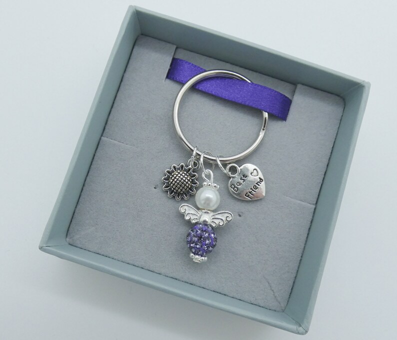 May include: A silver key chain with a purple crystal angel charm, a sunflower charm, a pearl bead, and a heart charm that says "Best Friend".