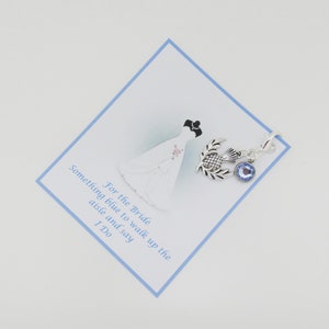 K&ouml;nnte beinhalten: Ein silberner Anh&auml;nger mit einem blauen Kristall und einem Distel-Design. Der Anh&auml;nger ist an einer Karte befestigt, auf der steht: "F&uuml;r die Braut Etwas Blaues, um den Gang entlang zu gehen und Ja zu sagen."