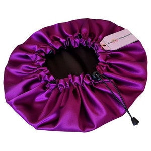 Op de afbeelding: Een paarse satijnen slaapmuts met een trekkoord en een label met de tekst "Bonita's Satin Bonnet".