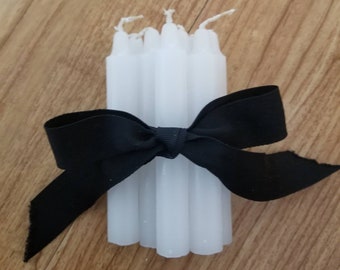 May include: A bundle of white taper candles tied together with a black ribbon.