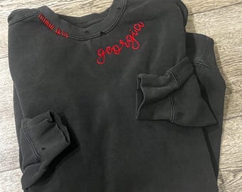 May include: A black sweatshirt with a red embroidered word "Georgia" on the front. The sweatshirt has a distressed look with some fraying around the neckline.