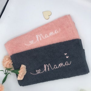 May include: Two towels, one pink and one gray, with the word "Mama" embroidered on each. The pink towel has a white heart, and the gray towel has two pink hearts.