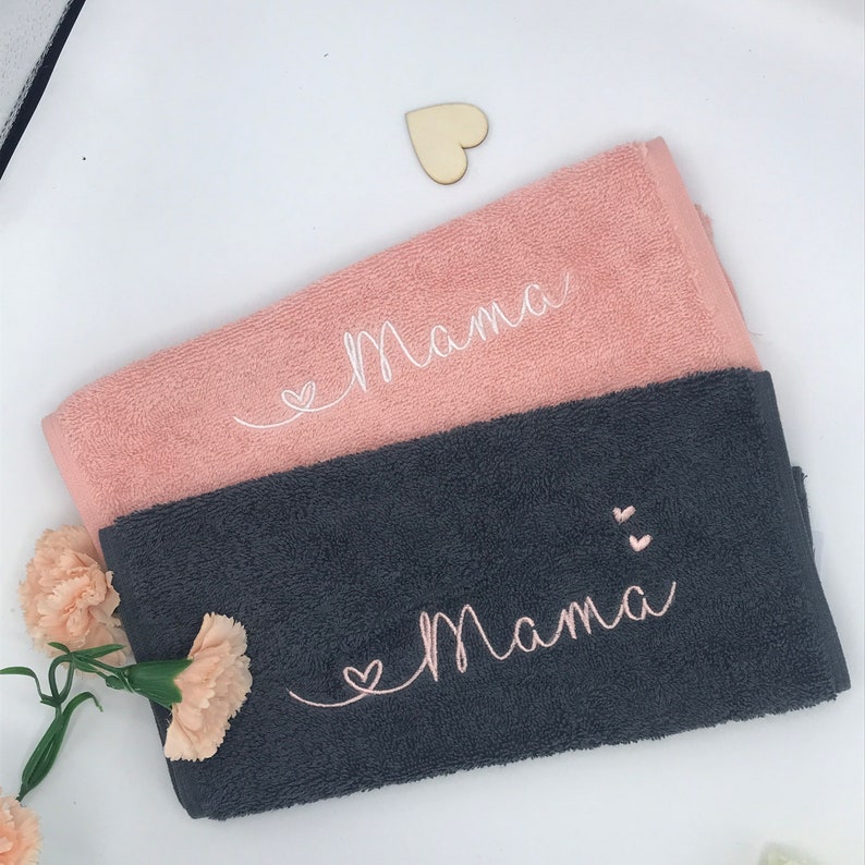 May include: Two towels, one pink and one gray, with the word "Mama" embroidered on each. The pink towel has a white heart, and the gray towel has two pink hearts.