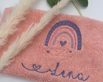 May include: A pink towel with a purple and pink rainbow embroidered on it. The rainbow has a small heart in the center and there are smaller hearts scattered around it. The name "Elena" is embroidered in purple below the rainbow.