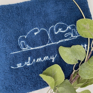 May include: A navy blue towel with white embroidered text and a boxing glove design. The word "Mom" is above the name "Jimmy" in cursive, with a small heart. Green leaves and a gold ring are in the background.