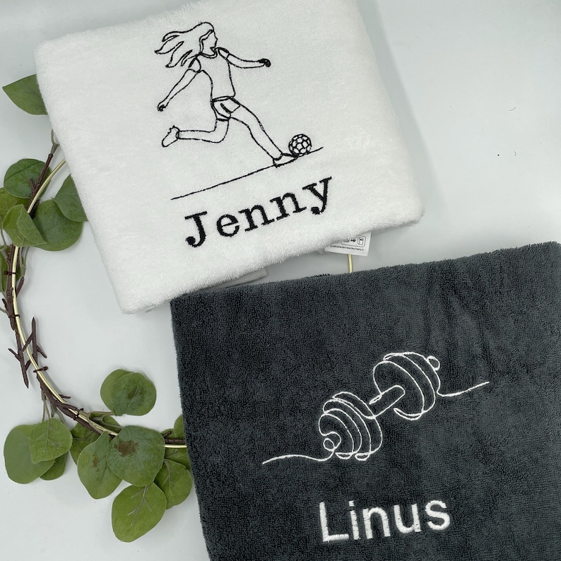 May include: Two personalized towels. One white towel features a soccer player graphic and the name "Jenny" embroidered in black. The other is a dark gray towel with a dumbbell graphic and the name "Linus" embroidered in white.