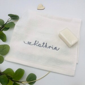 May include: White hand towel with a gray embroidered heart and the name "Kathrin" on a white background.
