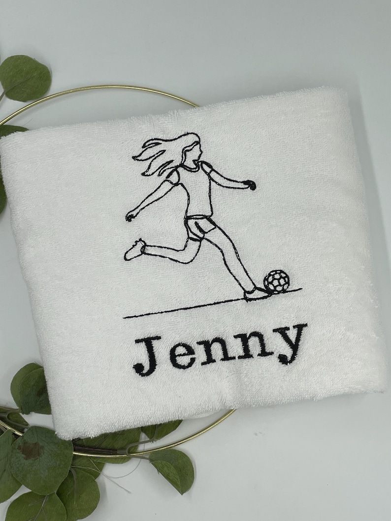 May include: White towel with a black embroidered soccer player kicking a soccer ball. The name "Jenny" is embroidered in black below the soccer player.