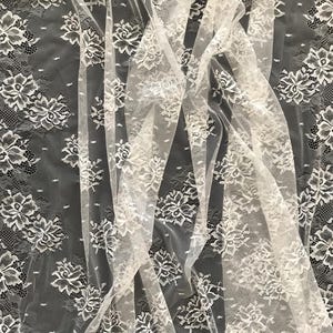 Puede incluir: Tela de encaje blanco con un diseño floral. El encaje presenta un diseño repetido de flores y hojas, con un borde festoneado. La tela es semitransparente, permitiendo el paso de la luz. Ideal para proyectos de costura.