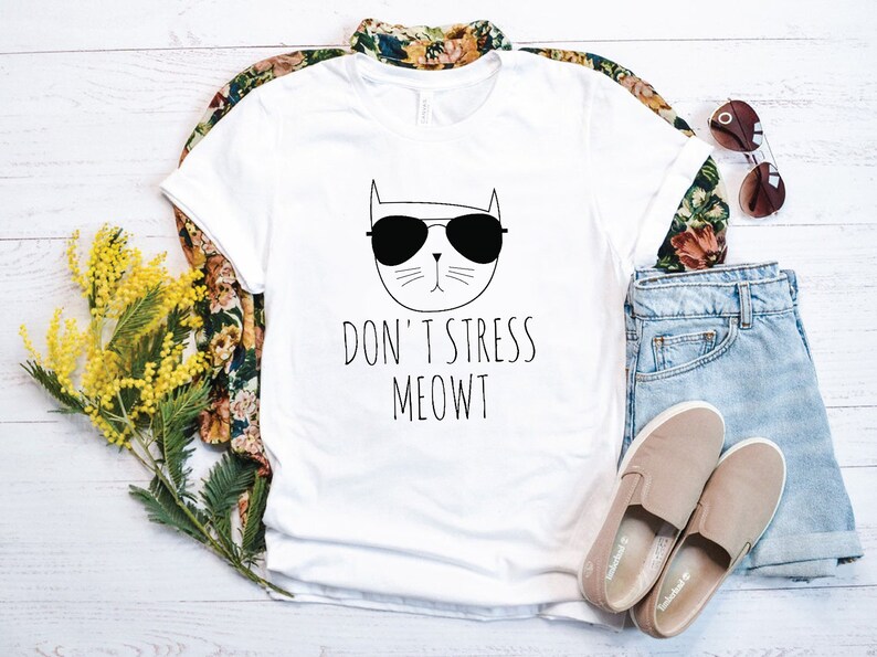 May include: White t-shirt with a black and white illustration of a cat wearing sunglasses. The text "Don't Stress Meowt" is printed below the cat.