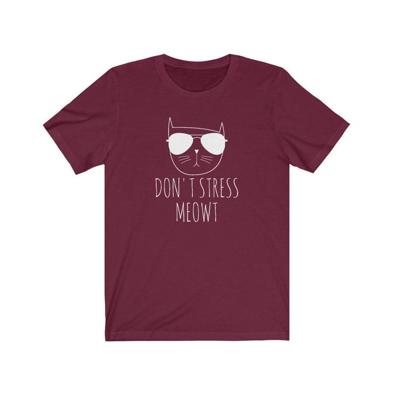 May include: Burgundy short-sleeved t-shirt with a white graphic of a cat wearing sunglasses and the text "Don't Stress Meowt".