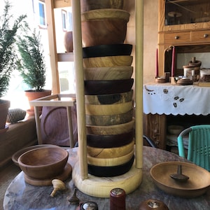 Könnte beinhalten: Ein Holzständer mit einem Stapel Holzschalen in verschiedenen Brauntönen, Schwarz und Rot. Der Ständer steht auf einem Marmortisch mit mehreren Holz-Drehscheiben.