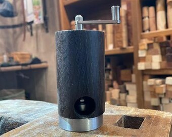 Könnte beinhalten: Ein schwarzer Pfeffermühle aus Holz mit einer silbernen Kurbel und einem silbernen Sockel. Die Mühle steht auf einer Holzoberfläche.