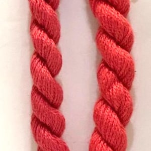 May include: Two skeins of vibrant watermelon-colored yarn, tightly wound and displayed vertically. Each skein is labeled with product information. The yarn is a rich, solid color, perfect for knitting or crocheting projects.