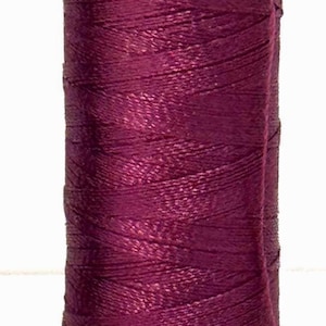 May include: A spool of dark burgundy rayon thread, labeled "100% Rayon 40wt." The spool has the numbers "942 1300" and the code "T286" printed on it. The thread is tightly wound.