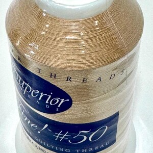 May include: A spool of beige Superior Threads So Fine quilting thread. The spool is labeled with the text "Superior Threads So Fine! #50 Quilting Thread 3,280 yds. Multifilament Polyester" and the number "406".