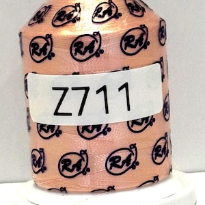 May include: A spool of peach-colored thread with a repeating black logo pattern. The spool has a white label with the text "Z711" in black. The thread is on a white base.