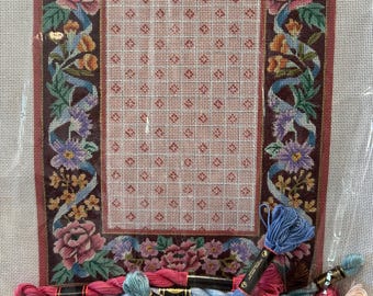 May include: A needlepoint kit with a floral design and a variety of colored embroidery floss. The kit includes a canvas with a pre-printed design, a needle, and a selection of floss in different colors.